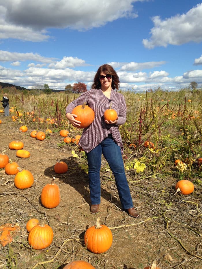 Shannon holding two pumpkins in a pumpkin field.